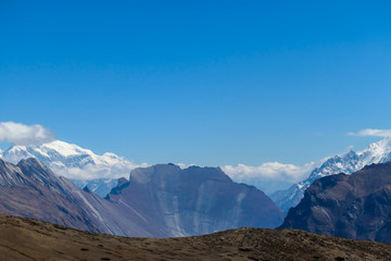 A panoramic view on steep Himalayan slopes along Annapurna Circuit Trek, Nepal. High, snow caped Annapurna peaks in the back catching the sunbeams. Serenity and calmness. Idyllic landscape.