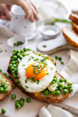 Vegetarian sandwich made of sourdough bread with the addition of fried egg and stewed green peas on a white board, close up view