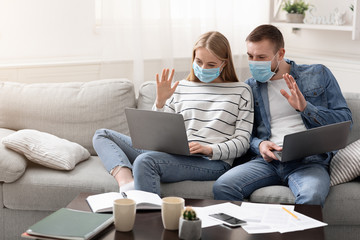 Working at home couple in protective masks greeting colleagues via laptop