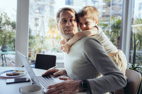 Boy hugging his father working on laptop at home