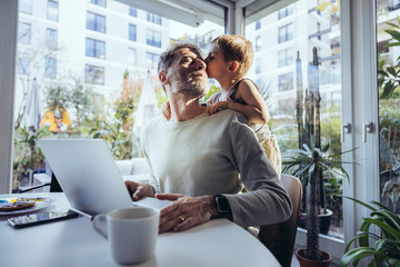 Little boy hugging father from behind, while working from home