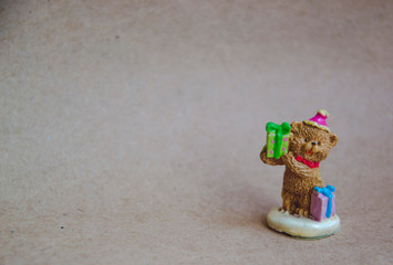 Small statue of bear with gifts for birthday on brown background. Greeting card with empty space for text. Close up picture of small figurine. Mockup for notes.