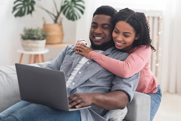 Cheerful black couple web surfing on laptop at home together