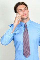 Portrait of young handsome businessman thinking while talking on the phone