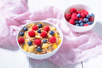 Bowl with granola, blueberries and raspberries in a white bowl, pink cloth on a white background. Healthy breakfast concept