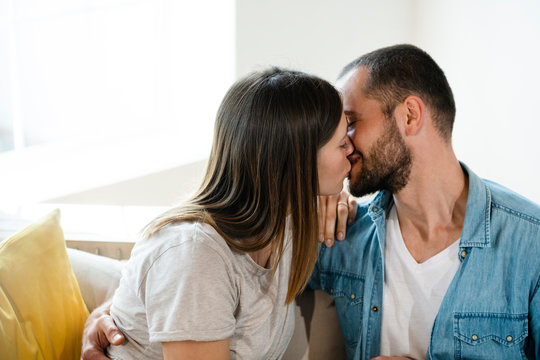 Affectionate young couple in love kissing on couch at home