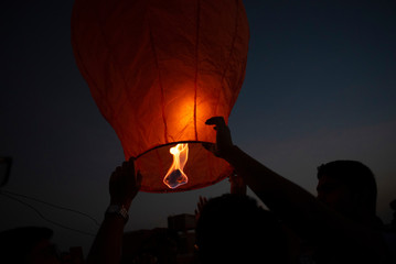 An Indian Bengali man celebrating Diwali by lighting flying lanterns in the sky in darkness. Indian lifestyle and Diwali celebration 
