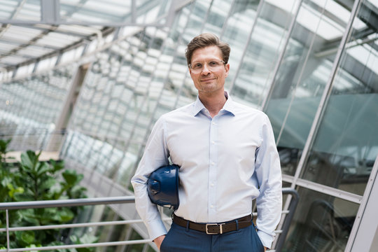 Architect with blue hard hat under his arm, standing in sustainable building