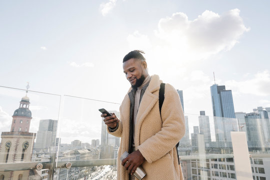 Stylish man using smartphone on observation terrace with skycraper view, Frankfurt, Germany