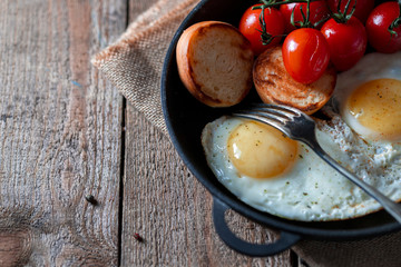 Fried eggs in a pan with cherry tomatoes and bread for breakfast. Breakfast concept. Wood background.