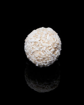 White coconut balls, raw and healthy sugar free rafaello candies on black glass background. Covering balls in coconut shred. Vegan, vegetarian sweets