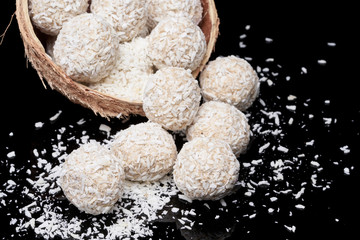 White coconut balls, raw and healthy sugar free rafaello candies on black glass background. Covering balls in coconut shred. Vegan, vegetarian sweets