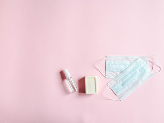 Flat lay personal protective equipment against various viruses - medical masks, bottle sanitizer and piece soap on pink background. Copy space.