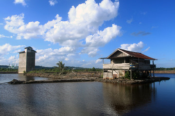 Fototapeta na wymiar Abandone house on the fish pond. with beautiful clouds and blue sky.