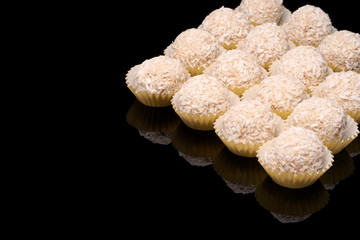 White coconut balls, raw and healthy sugar free rafaello candies on black glass background. Covering balls in coconut shred. Vegan, vegetarian sweets