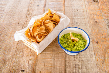 Guacamole with tortilla chips on light wooden table