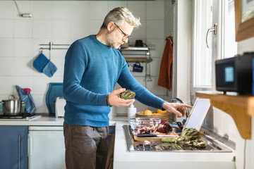 Mature man preparing salad in his kitchen using digital tablet