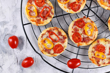 Small mini pizzas topped with cheese, tomato, yellow and red bell peppers and salami sausage on round black grid side