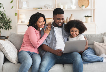 Loving African American Family Of Three Resting On Couch With Laptop