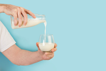 Fototapeta na wymiar Hombre con una botella de leche en la mano sirviendo en un vaso sobre un fondo celeste. Vista de frente. Copy space
