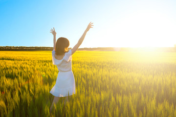 Beautiful caucasian woman in white dress jumping up with raised hands outdoor. Field with yellow wheat around