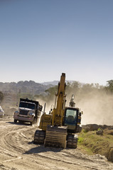 An industrial dump truck transporting dirt in a construction site next to a backhoe.