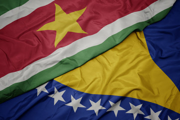 waving colorful flag of bosnia and herzegovina and national flag of suriname.