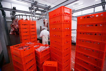 A lot of plastic red boxes with chopped fresh raw meat, a worker arranged a stored in a meat...