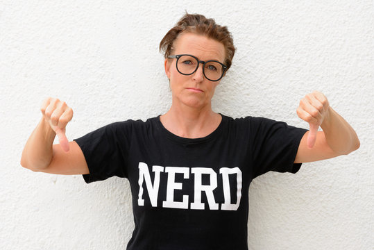 Mature nerd woman wearing big eyeglasses and standing against white background outdoors while giving thumbs down