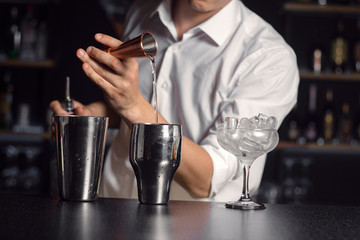 Process of making cocktail by male bartender.Pouring liquid ingredient out of measure cup into cocktail shaker.