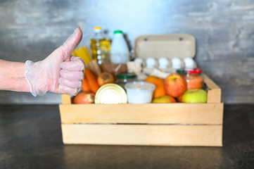 Volunteer hands in medical gloves holding donation box with various products for poor people. Pandemic coronavirus food shortages. Food donations or delivery concept. Free space for text copyspace