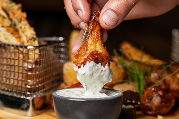 Hand holding grilled chicken legs dipping in sauce and set of grilled black pepper chicken...