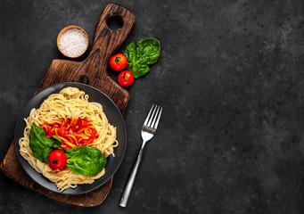 
Italian pasta spaghetti with tomato sauce and herbs on a black plate on a stone background with copy space for your text