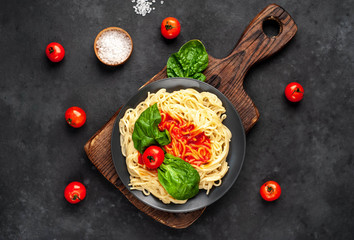 Fototapeta na wymiar Italian pasta spaghetti with tomato sauce and herbs on a black plate on a stone background