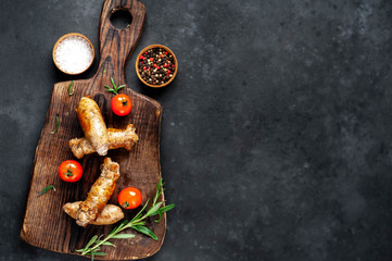 Fototapeta na wymiar Grilled sausages with spices, tomatoes, rosemary on a stone background with copy space for your text