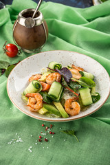 Shrimp salad with cucumber, avocado, lettuce and tomato on green background