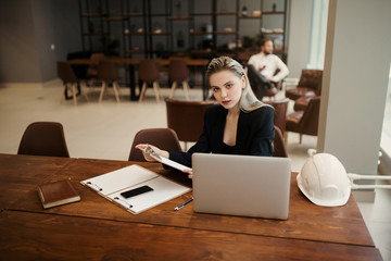 A lawyer girl in a classic suit sits at her Desk with a laptop in a coworking office and looks directly at the camera