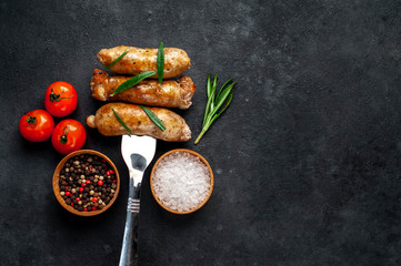 Grilled sausage on a fork with spices, tomatoes on a stone background with copy space for your text
