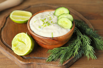 Delicious yogurt sauce with cucumber in bowl on wooden table