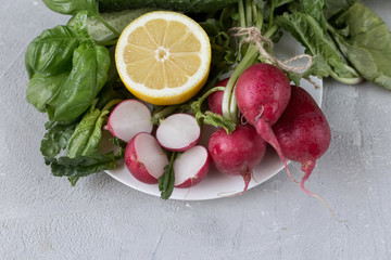 
Fresh vegetables on a gray background are laid out, cabbage, lemon, radish, spinach, cucumbers. Close-up on a concrete gray background.