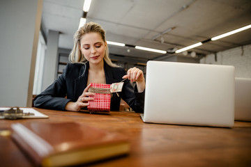 A beautiful blonde businesswoman sits at a Desk in the office and holds a gift that was given by colleagues at work