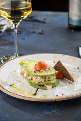 Starter with salmon tartare salad avocado and rye bread toast with glass of white wine on blue background