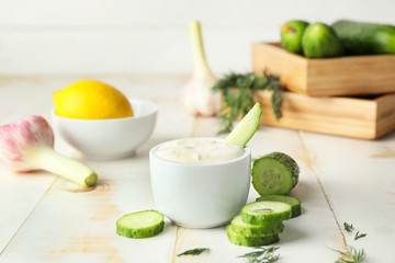 Delicious yogurt sauce with cucumber in bowl on white table