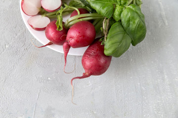 
Radish on a white plate, spinach, basil, gray light background