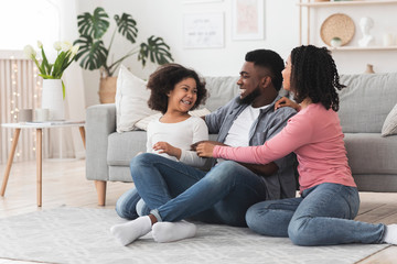 Cheerful african parents tickling their daughter while relaxing in living room