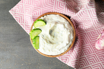 Delicious yogurt sauce with cucumber in bowl on grey background