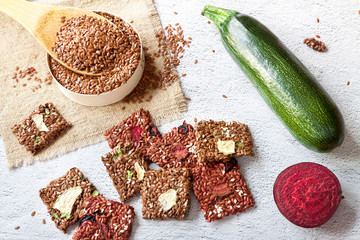 Flat lay top view crunchy flax seeds crispbread and raw round beetroot and zucchini on white background. Healthy snack: multigrain cereal flax seed with dry vegetables, sesame, , flaxseeds on wooden