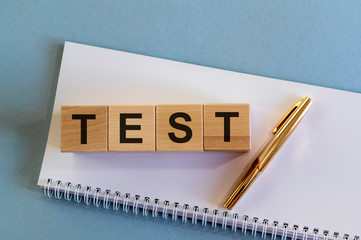 Test word on wooden cubes on notepad with pen on light blue background