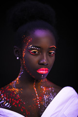 awesome african model in neon light, unusual interesting portrait of beautiful girl with fluorescent makeup on whole body. isolated dark background