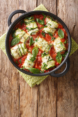 Mediterranean zucchini rolls with ricotta and herbs baked in tomato sauce in a pan close-up. vertical top view